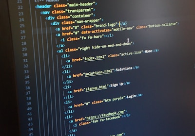 A computer monitor displays HTML code in an integrated development environment. The screen shows a structured hierarchy of HTML tags, including elements such as header, nav, and list items with classes and hyperlinks.